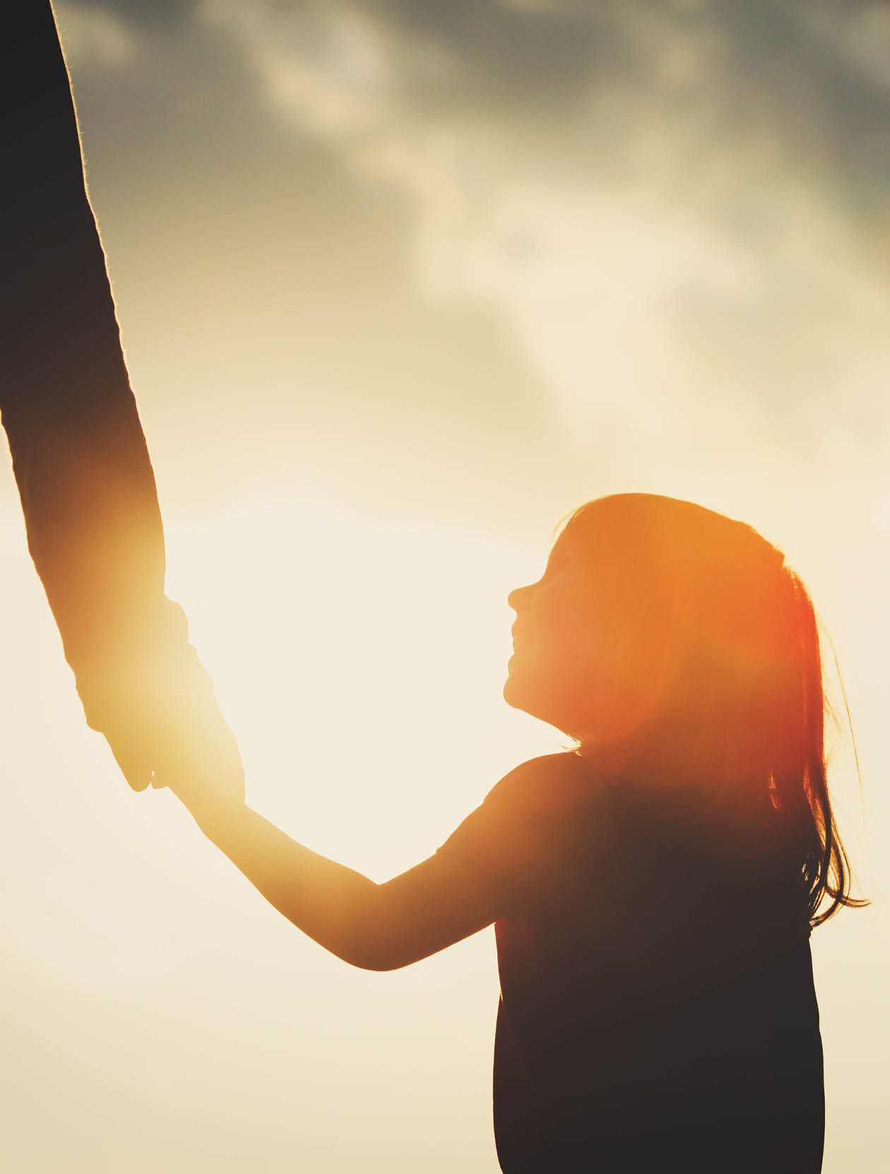 silhouette of little girl holding parent hand at sunset sky